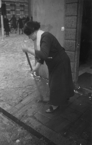 221105 Afbeelding van een vrouw die de natte sneeuw wegveegt van de stoep voor haar huis in de binnenstad van Utrecht.